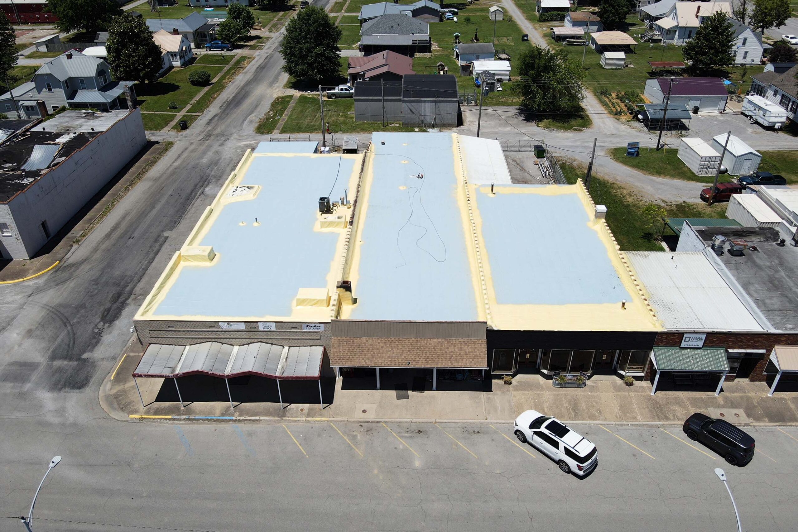 Aerial view of a cool roofing system being applied to the roof of a business by ArmorGuard.